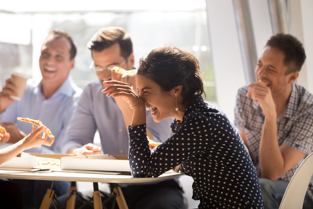 Indian woman laughing at funny joke eating pizza with diverse coworkers in office(fizkes)S