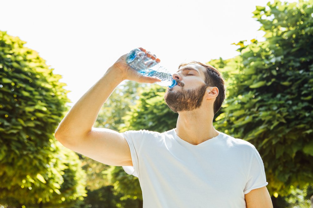 Close up of a man drinking water from a bottle outside