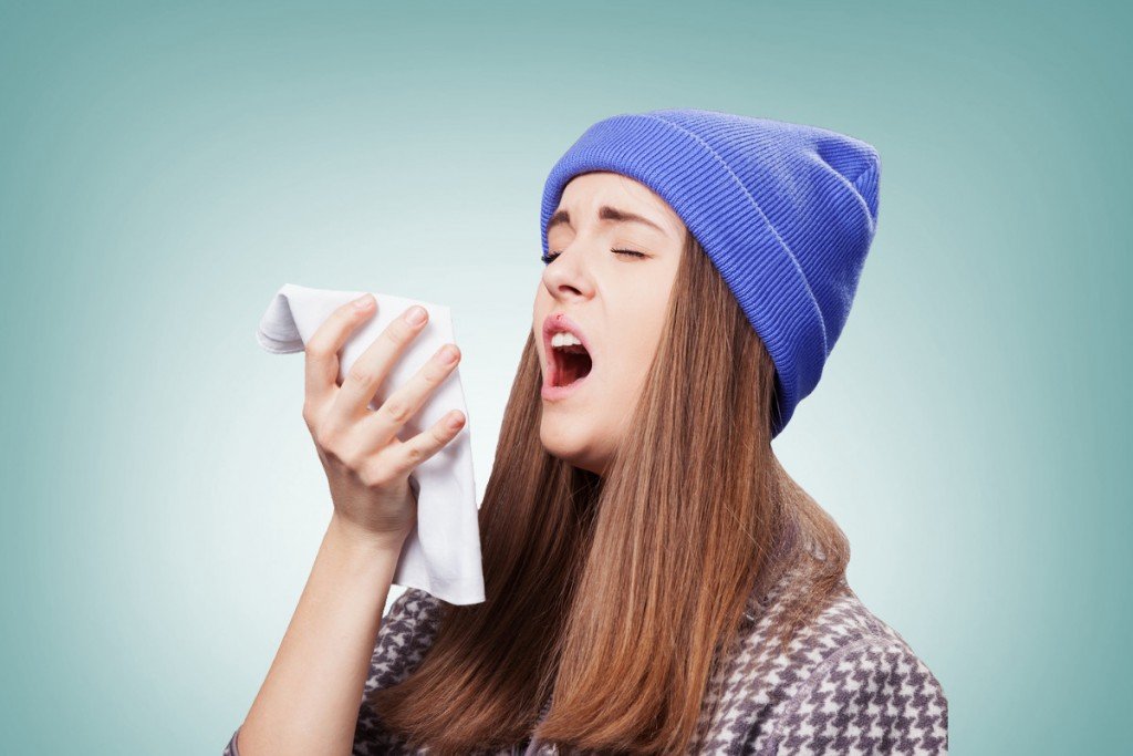 Sick young woman with a flu, sneezing closeup over grey