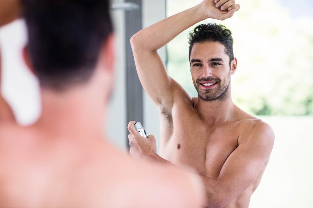 Handsome shirtless man putting deodorant in the bathroom