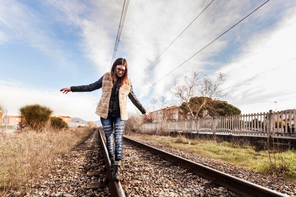 Beautiful Young Woman Walking in Balance on Railway Tracks. The Railroad is in a Residential Area. The Girl has a Casual Look.