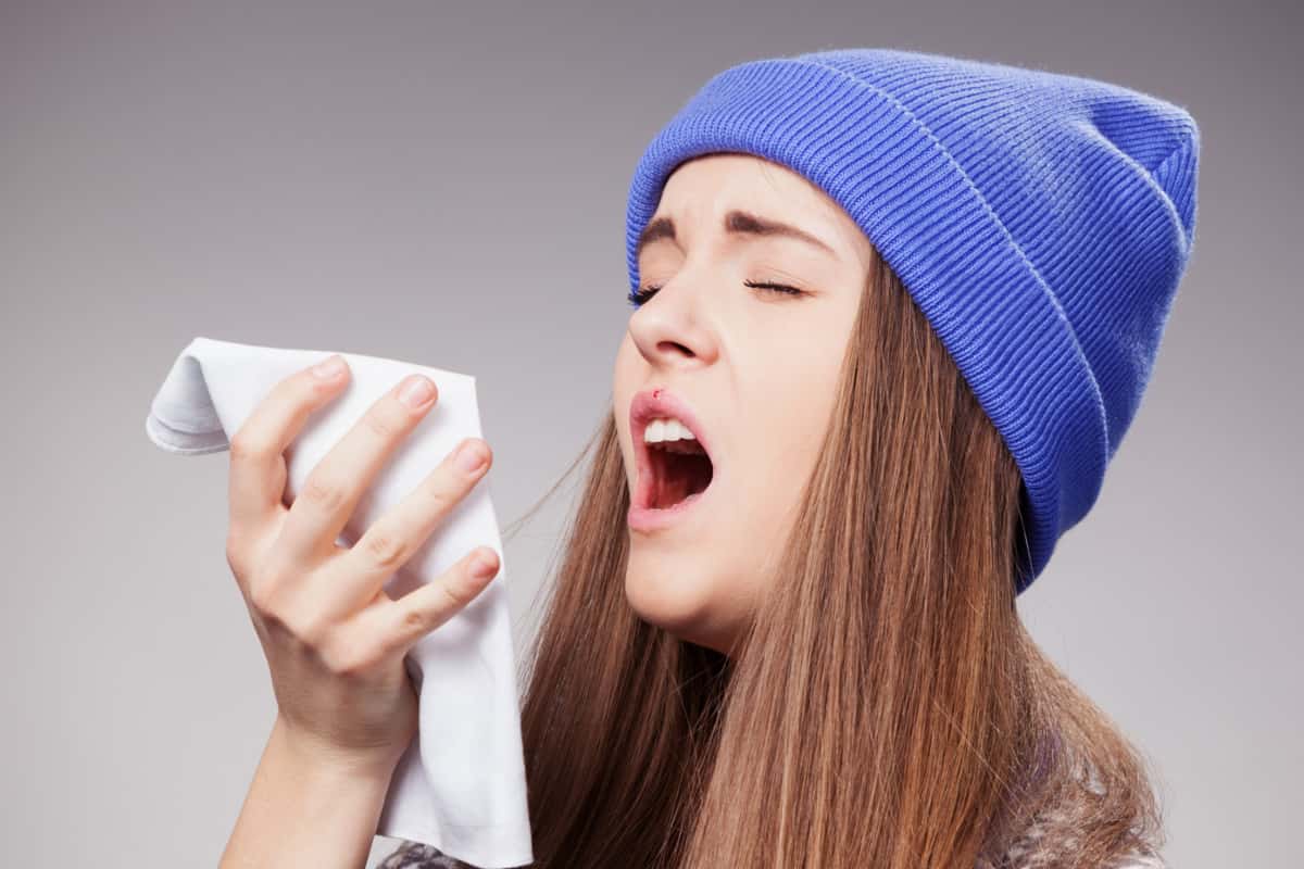 Sick young woman with a flu, sneezing closeup over grey