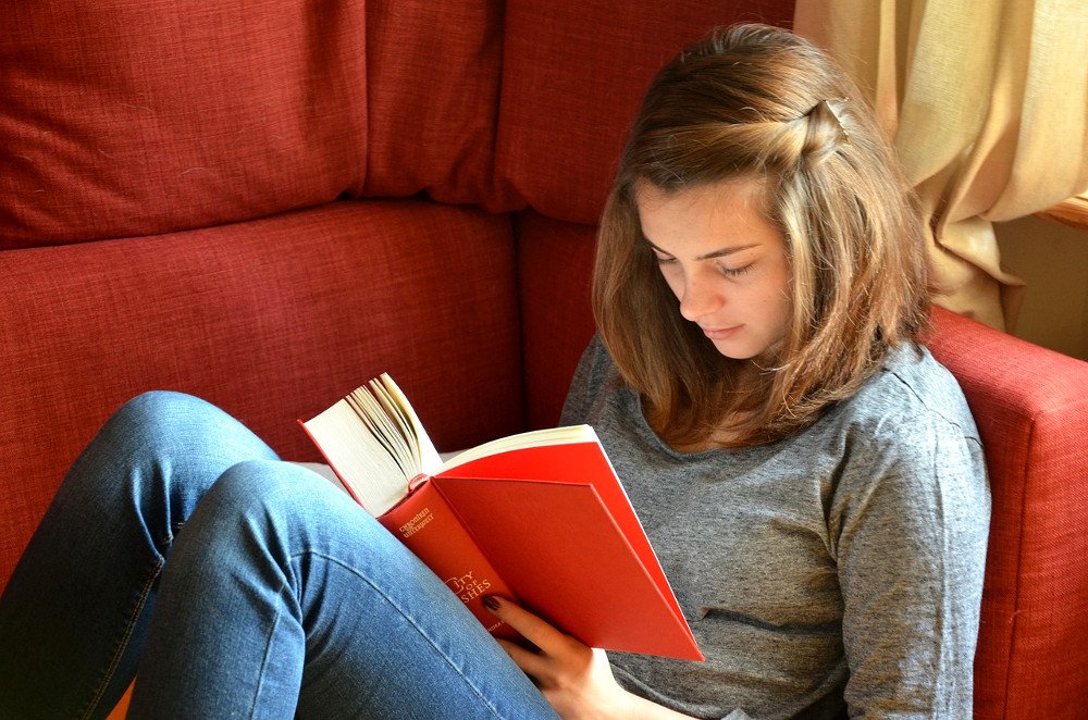 Young girl reading orange cover book on sofa