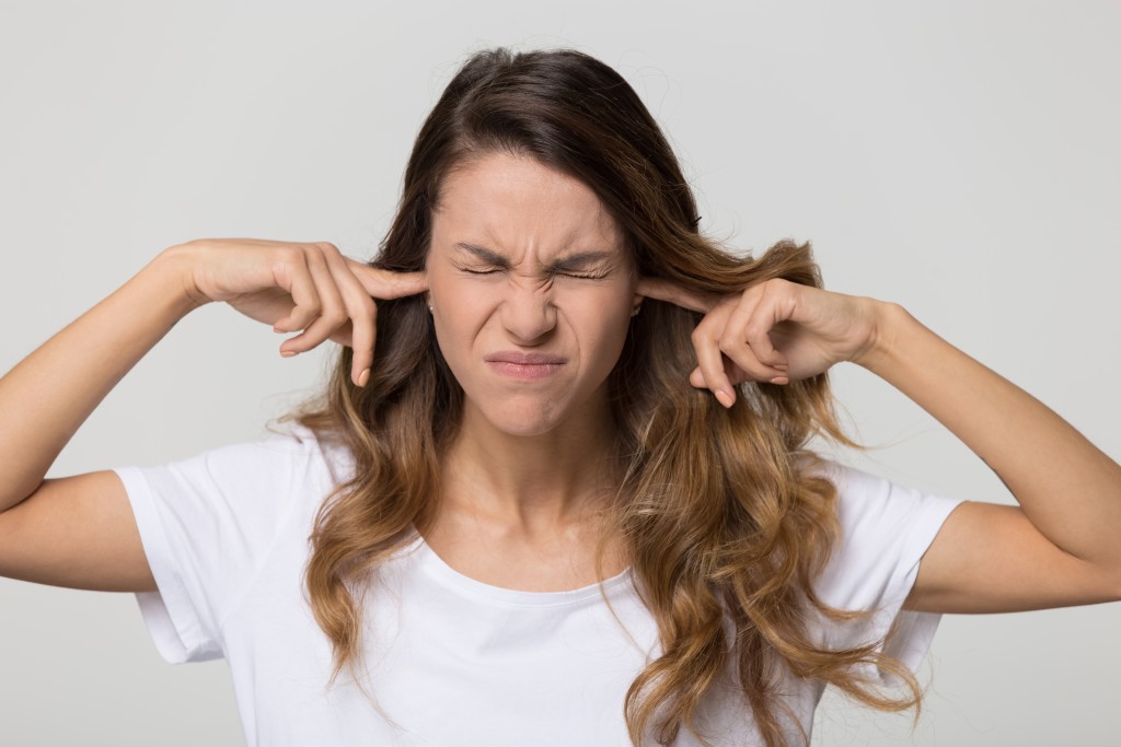 Stubborn annoyed woman sticking plug fingers in ears not listening to loud noise sound isolated on white blank studio background, young angry teen refuse hear avoid stress feel ear pain ache concept - Image