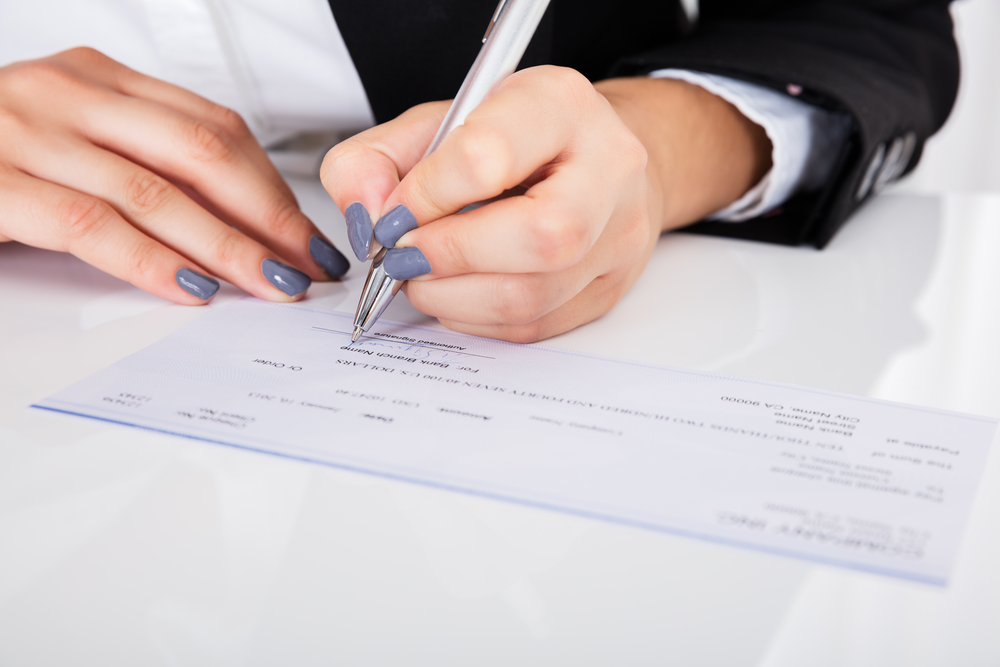 Close-up Of Person's Hand Signing Cheque On Desk - Image( Andrey_Popov)s