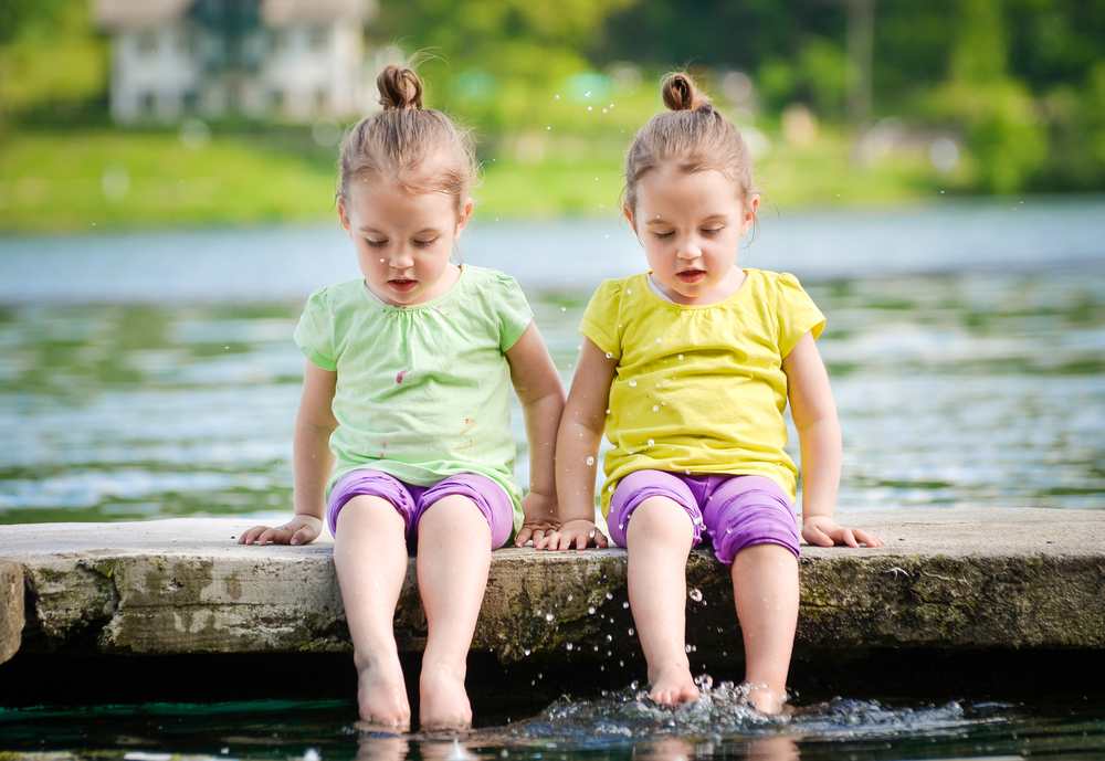 Identical twins girls are exercising on lake shore, sprinkling water. Children sitting on lake side, playing with water. Healthy and active children lifestyle. - Image(JGA)s