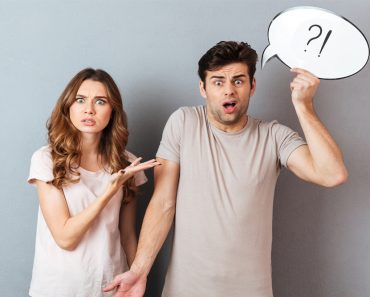 Portrait of a young frustrated couple having an argument while standing and holding speech bubble isolated over gray wall - Image(Dean Drobot)s