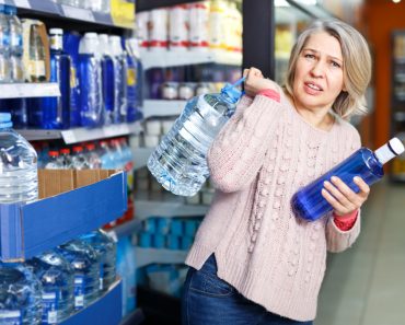 Tense modern woman lifting heavy bottle of still water while shopping at grocery store - Image( Iakov Filimonov)s