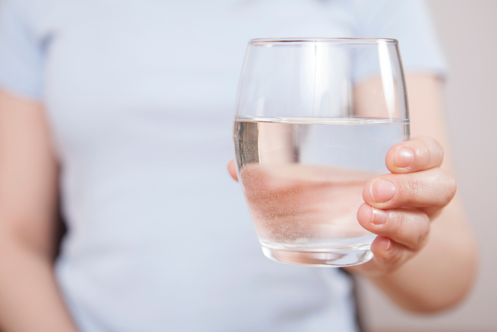 Woman is hand holding drinking water on gray background - Image( Busra Ispir)S