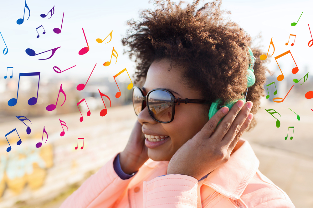 technology, lifestyle and people concept - smiling african american young woman or teenage girl in headphones listening to music outdoors over colorful musical notes background - Image( Syda Productions)s