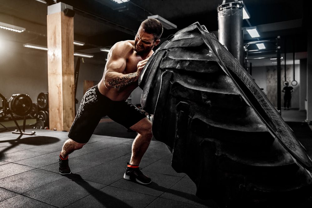 Shirtless man flipping heavy tire at gym - Image( Oleksandr Zamuruiev)s