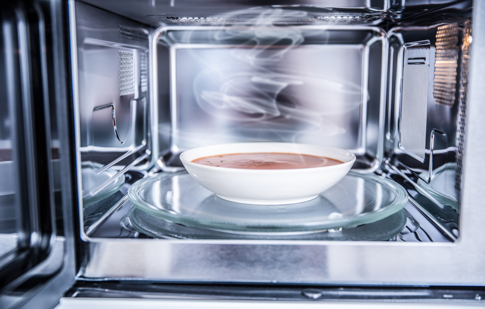 Inside view of new clean staniless microwave oven with a tomato soup in white plate( Marian Weyo)s