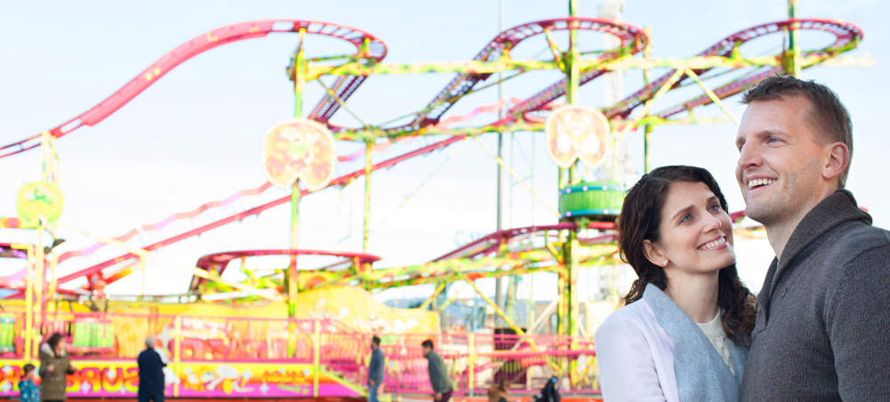 Panoramic view of beautiful tourist couple visiting colorful amusement park with roller coaster ride(MJTH)s