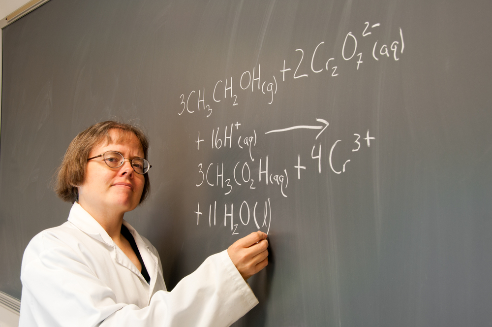 A woman chemistry instructor writes out a chemical equation on a chalk board(Erika J Mitchell)S