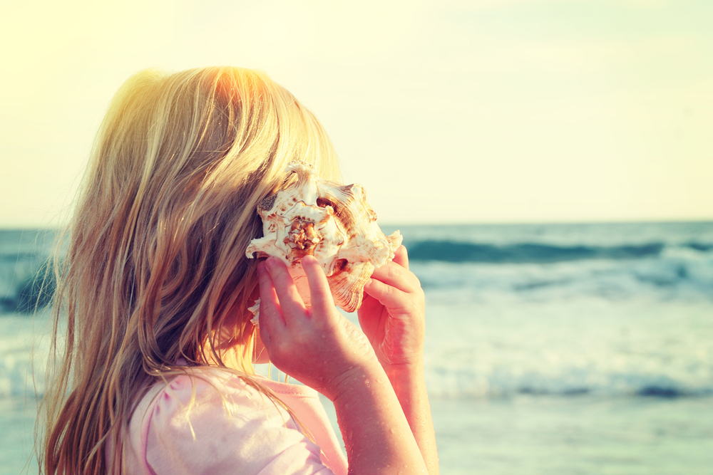 Happy little girl listen to seashell at the beach(Guschenkova)s