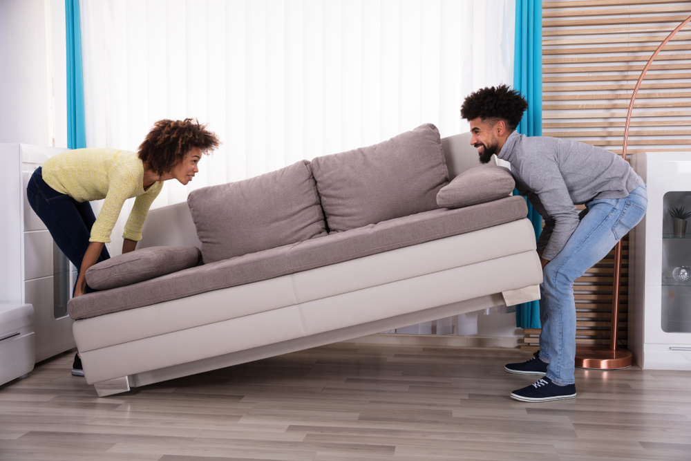 Side View Of Young Smiling Couple Lifting Sofa In Living Room(Andrey_Popov)S