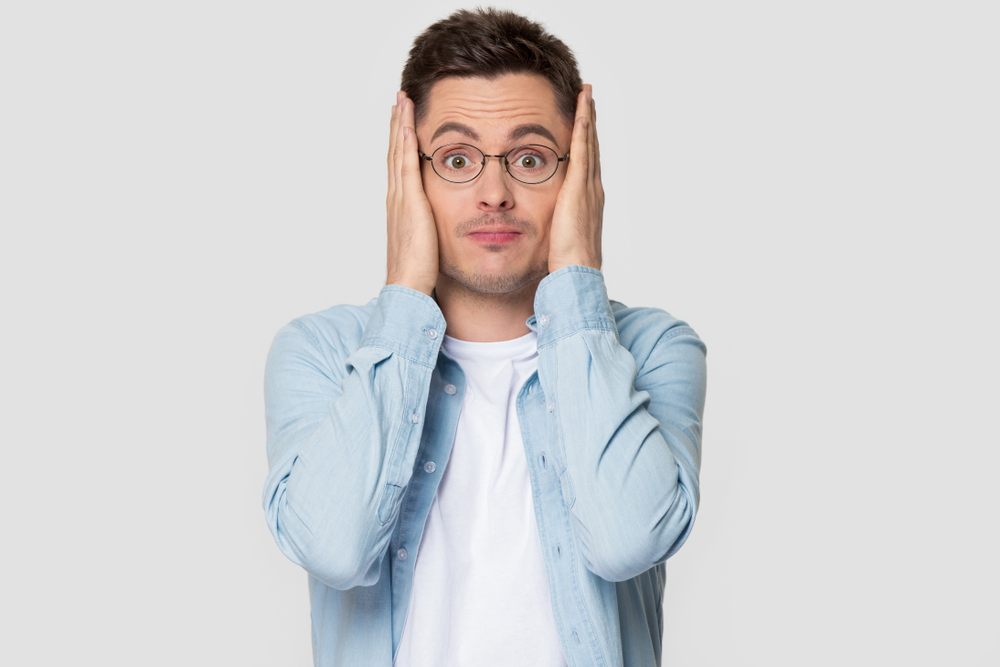 Funny worried man in glasses jean shirt hold head in hands looks concerned pose studio grey wall(fizkes)S