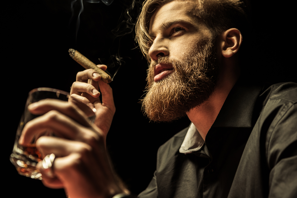 Handsome bearded man holding glass of whisky and smoking cigar(LightField Studios)s