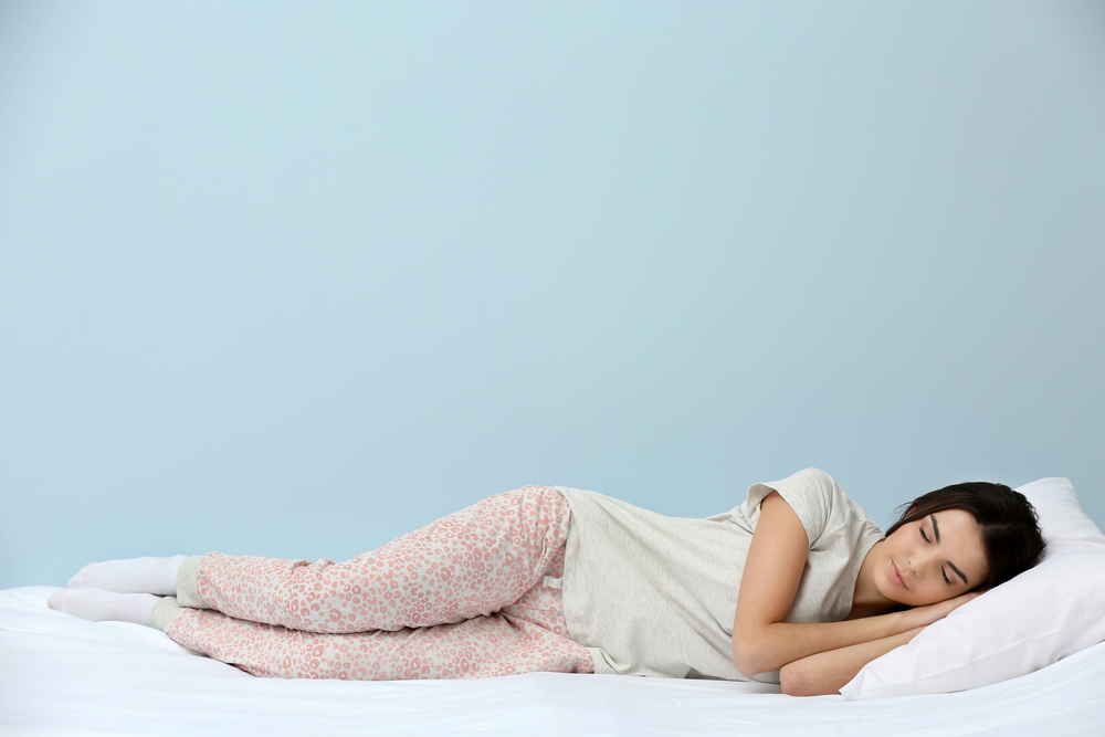Young woman in pajamas sleeping on bed on blue background(Africa Studio)S