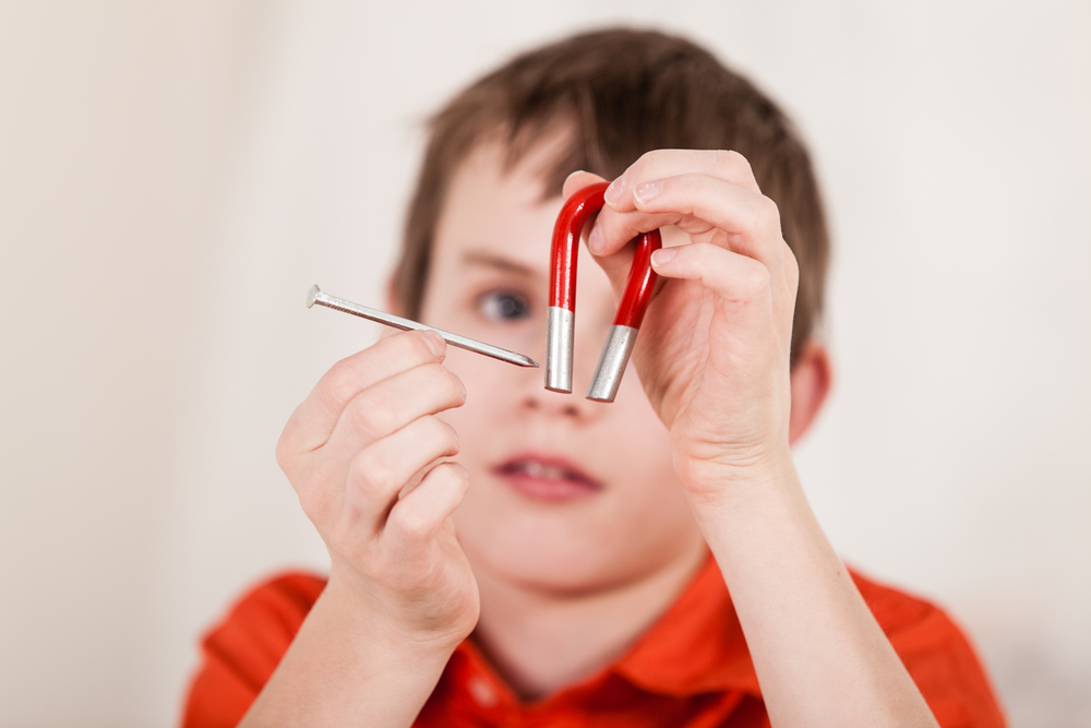 Selective focus close up on hands of boy moving large iron nail next to red and white magnet(Jan H Andersen)S