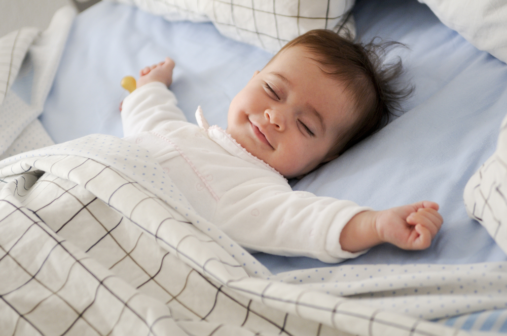 Smiling baby girl lying on a bed sleeping on blue sheets(javi_indy)S