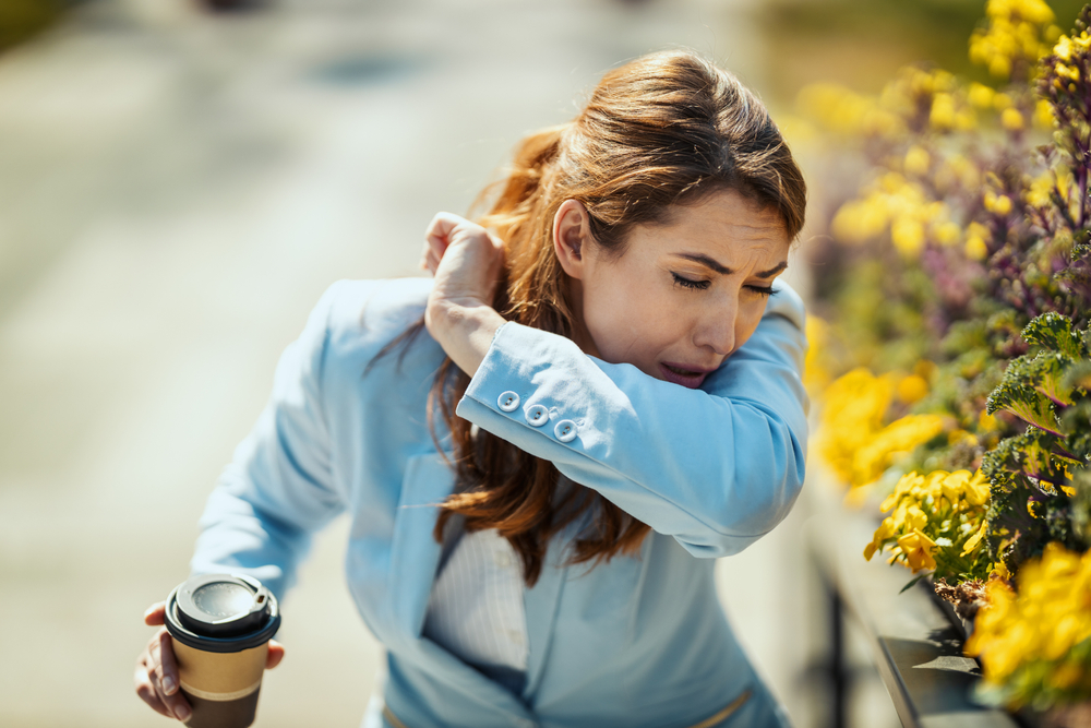 A young businesswoman on a coffee break outside is sneezing into the elbow by an allergy or a cold(MilanMarkovic78)s