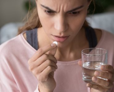 Serious stressed sick millennial mixed race woman holding and thinking over taking round white pill and glass of water(fizkes)s