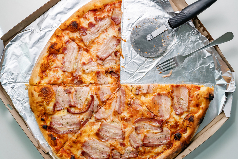 Close up on bacon and cheese pizza with two slices one quarter taken with metal fork(Miljan Zivkovic)S