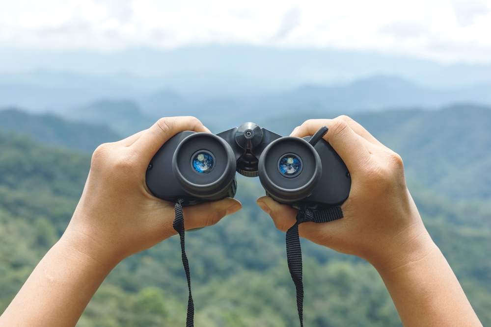 Hands,Holding,Binoculars,On,Mountains,Background