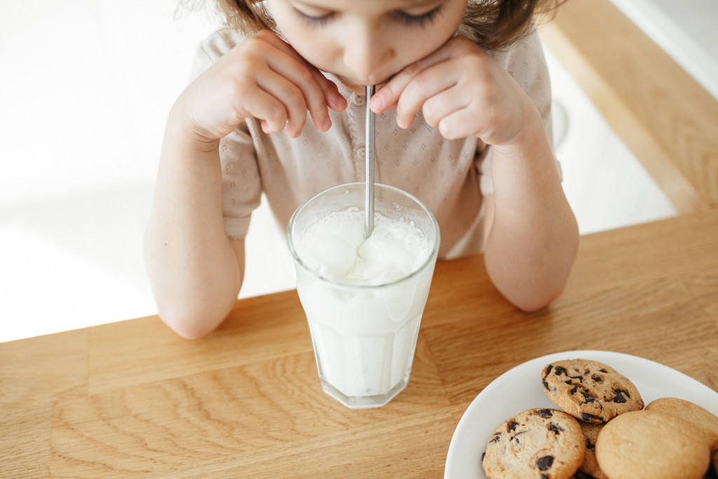 cute-5-year-girl-drinking-milk-with-steel-straw-from-glass-and-eating-cookies-sitting-at-kitchen_t20_KJ9bx0