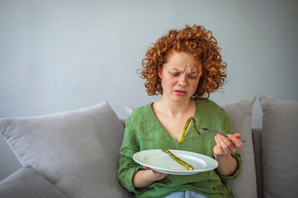 Girl keeping diet. Eating disorder. Cropped image of girl eating asparagus. Dieting habits changes. Woman hates vegetarian diet. Hungry on a diet. Displeased young woman eating green asparagus
