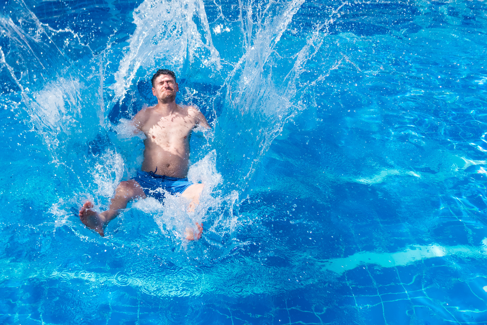 Man,In,Blue,Trunks,Jumping,In,The,Pool,With,Splashes