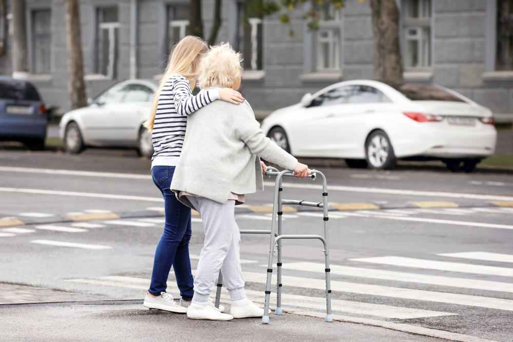 Young,Woman,Helping,Her,Elderly,Grandmother,With,Walking,Frame,To